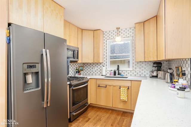 kitchen with appliances with stainless steel finishes, light brown cabinetry, a sink, light countertops, and backsplash