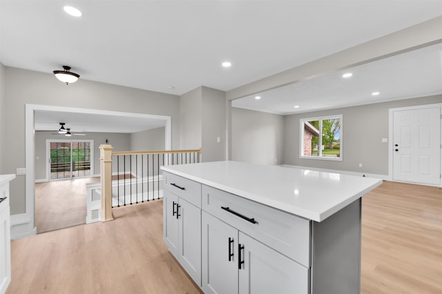 kitchen featuring a ceiling fan, light wood-type flooring, a kitchen island, light countertops, and open floor plan
