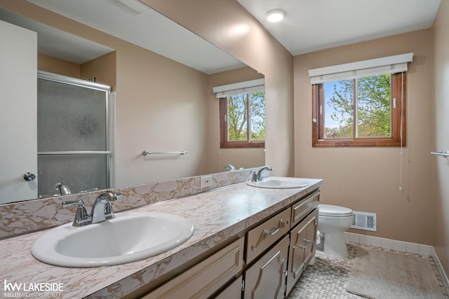 bathroom with toilet, a shower with shower door, double vanity, and baseboards