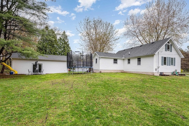 back of property featuring a trampoline, a lawn, and a shingled roof