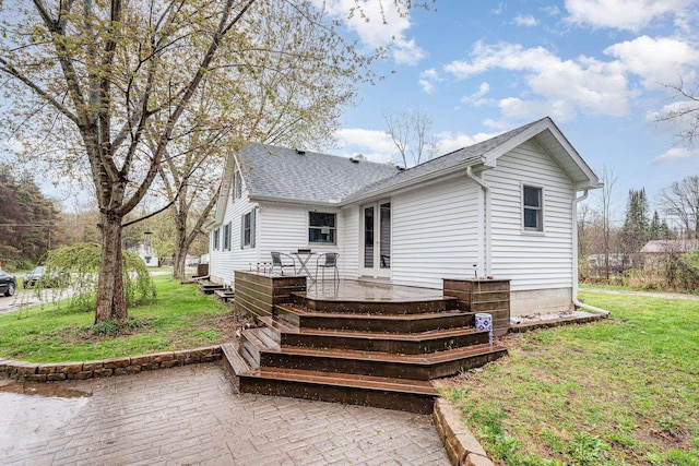 back of house with a patio, roof with shingles, and a lawn