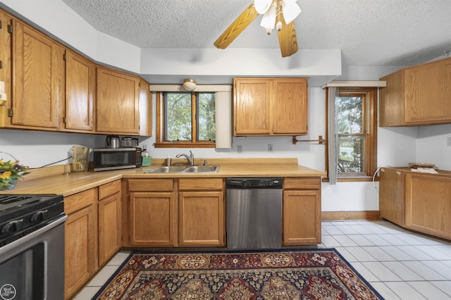 kitchen featuring stainless steel appliances, a sink, a textured ceiling, healthy amount of natural light, and light tile patterned floors