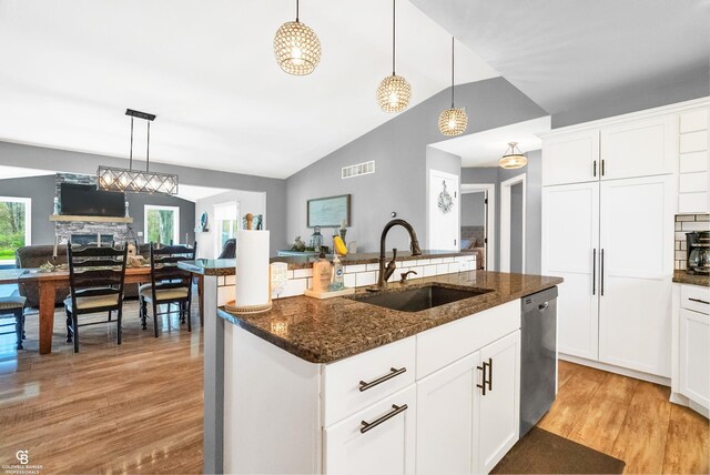 kitchen with a sink, stainless steel dishwasher, light wood-style floors, open floor plan, and dark stone countertops
