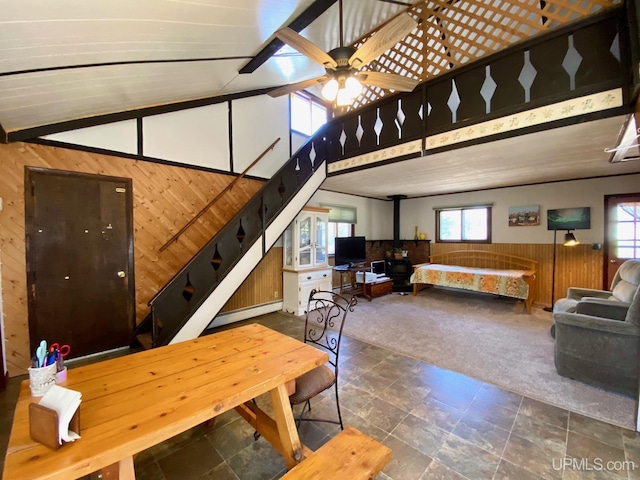 carpeted dining space with wood walls, stairway, high vaulted ceiling, stone finish floors, and ceiling fan