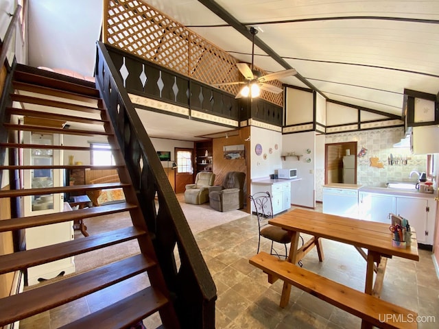 stairs featuring ceiling fan, stone finish floors, and high vaulted ceiling