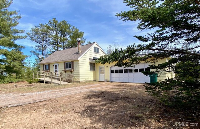 view of front of home featuring dirt driveway, an attached garage, and roof with shingles