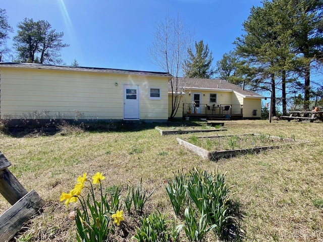 rear view of house with a garden, a wooden deck, and a lawn