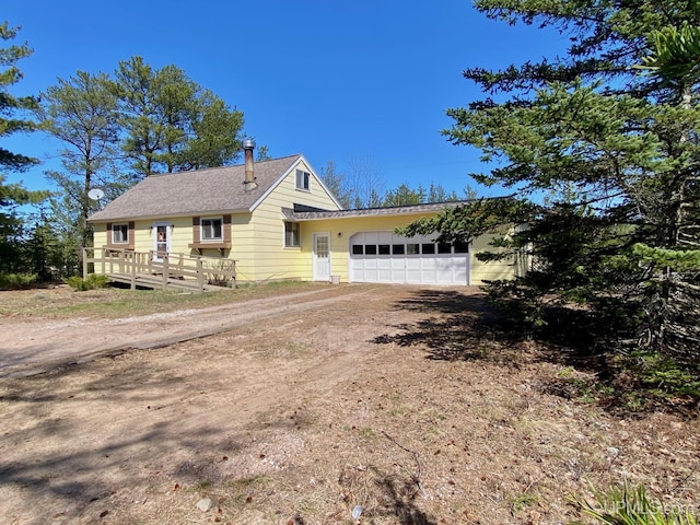 view of front of property with dirt driveway, an attached garage, a wooden deck, and roof with shingles