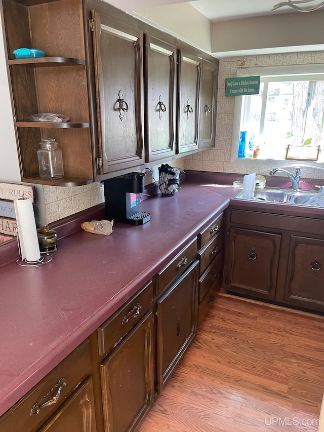 kitchen featuring a sink, open shelves, dark countertops, light wood-style flooring, and decorative backsplash