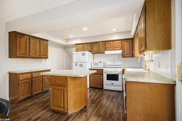 kitchen featuring white appliances, under cabinet range hood, a sink, dark wood-type flooring, and light countertops