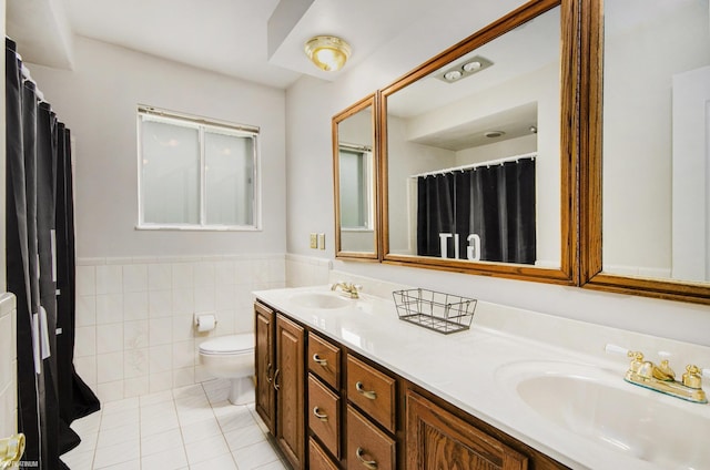 full bathroom featuring toilet, double vanity, wainscoting, tile patterned floors, and tile walls