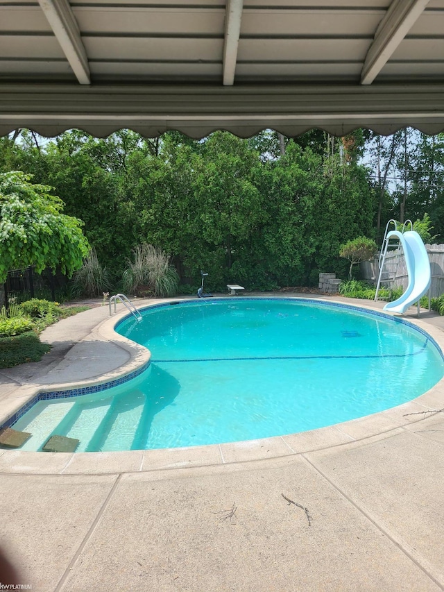 outdoor pool with a water slide, a patio area, and fence