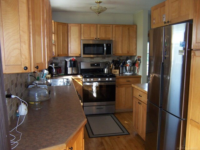 kitchen with stainless steel appliances, backsplash, and light wood-style flooring