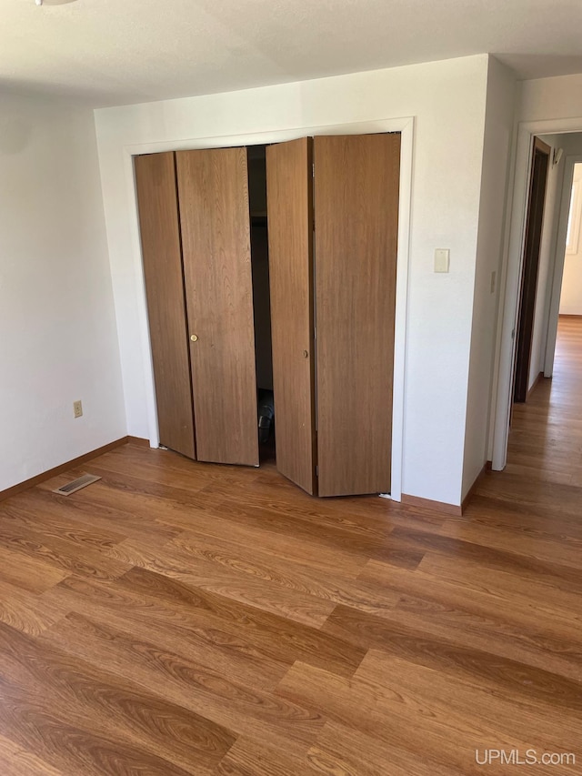 unfurnished bedroom featuring wood finished floors, a closet, and baseboards