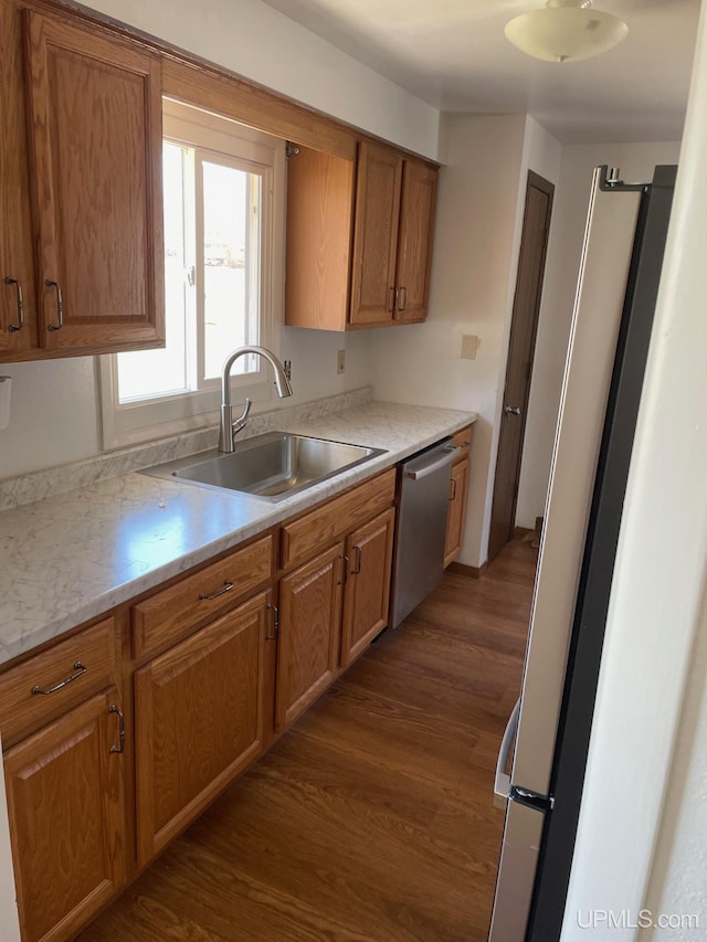 kitchen featuring appliances with stainless steel finishes, a sink, dark wood finished floors, light countertops, and brown cabinetry