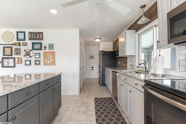 kitchen with stainless steel appliances, gray cabinets, a sink, a ceiling fan, and backsplash