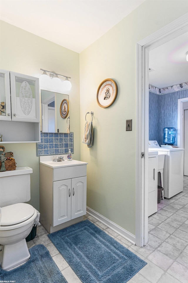 bathroom featuring washing machine and clothes dryer, vanity, toilet, and baseboards