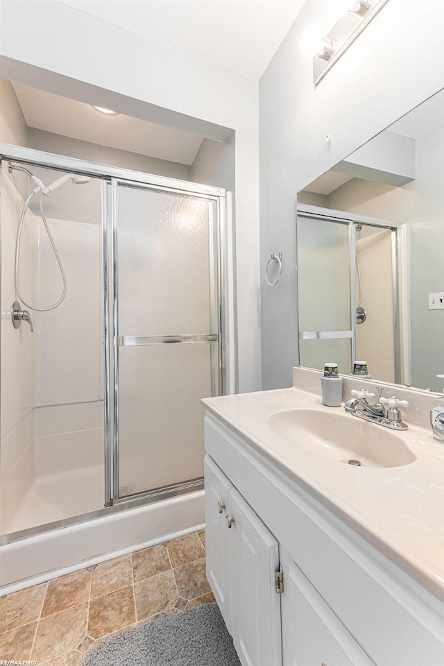 bathroom featuring stone finish flooring, a shower stall, and vanity