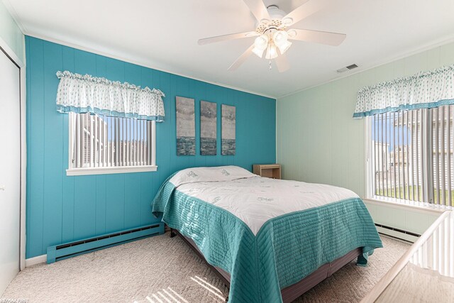 carpeted bedroom featuring baseboard heating, multiple windows, crown molding, and ceiling fan