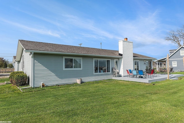 back of property with a patio area, a chimney, a lawn, and a shingled roof