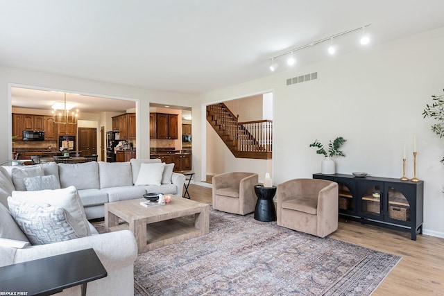 living room with light wood-type flooring, a chandelier, stairs, baseboards, and track lighting