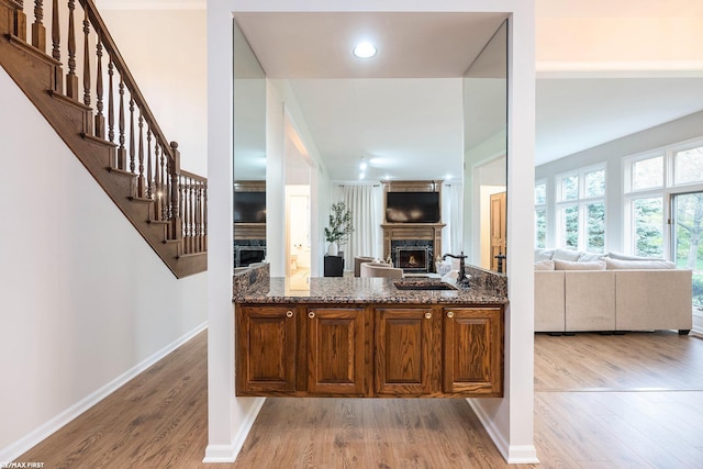 bar with a warm lit fireplace, light wood finished floors, baseboards, a sink, and stairway