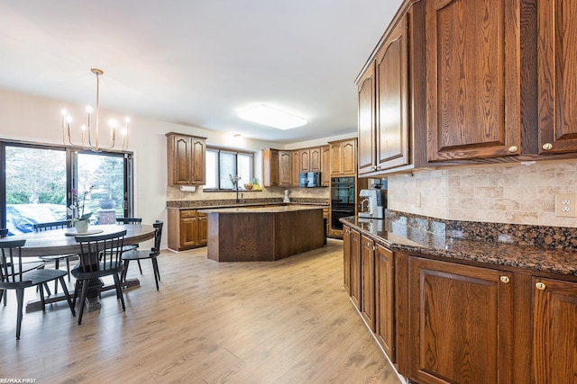 kitchen featuring black appliances, a chandelier, light wood-style flooring, backsplash, and a kitchen island