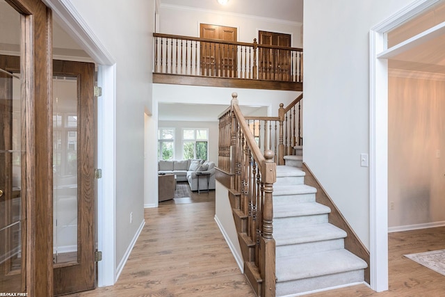 staircase with wood finished floors, baseboards, and ornamental molding