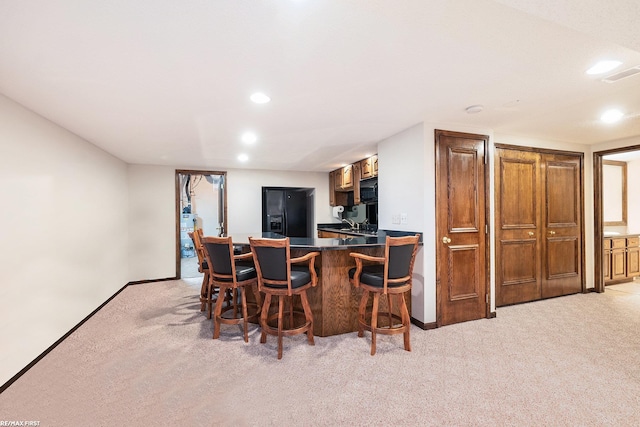 kitchen with black appliances, light colored carpet, recessed lighting, dark countertops, and a breakfast bar