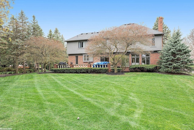 back of house featuring a lawn, brick siding, and a chimney