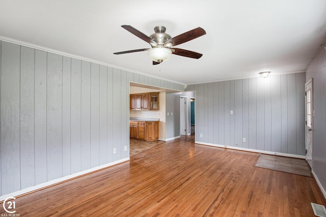 6424 Hunters Creek Rd, Imlay City, MI 48444 - unfurnished living room with light wood-type flooring, a ceiling fan, baseboards, wood walls, and ornamental molding