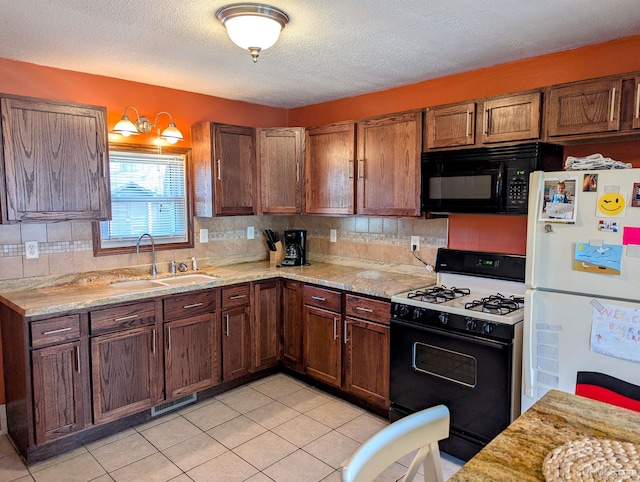 kitchen featuring gas range, freestanding refrigerator, a sink, black microwave, and decorative backsplash
