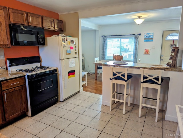 kitchen featuring black microwave, gas range oven, crown molding, a breakfast bar area, and freestanding refrigerator