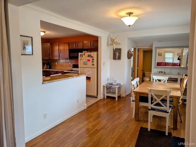 dining area with light wood finished floors, crown molding, and baseboards