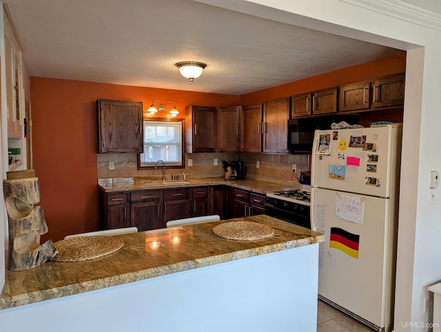 kitchen with freestanding refrigerator, gas range oven, a sink, black microwave, and decorative backsplash