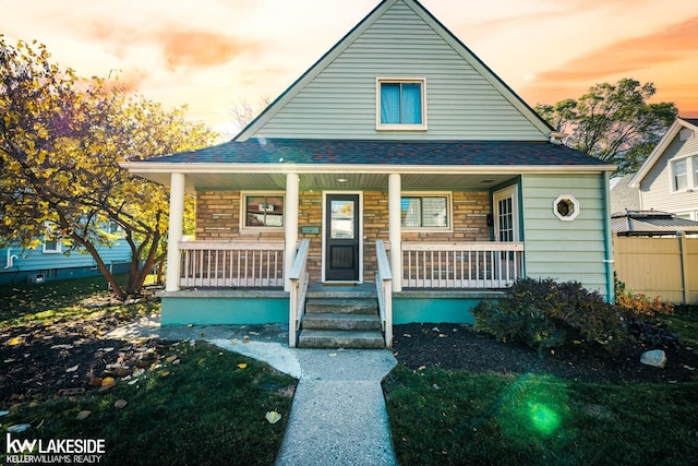 view of front facade featuring a porch, a shingled roof, and stone siding