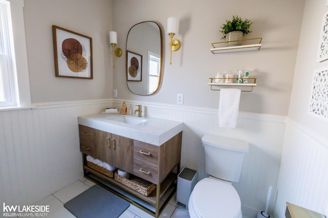 half bathroom with a wainscoted wall, toilet, vanity, and tile patterned flooring