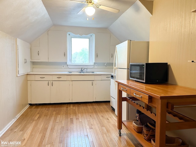 kitchen with stainless steel microwave, light wood-type flooring, light countertops, vaulted ceiling, and white cabinetry
