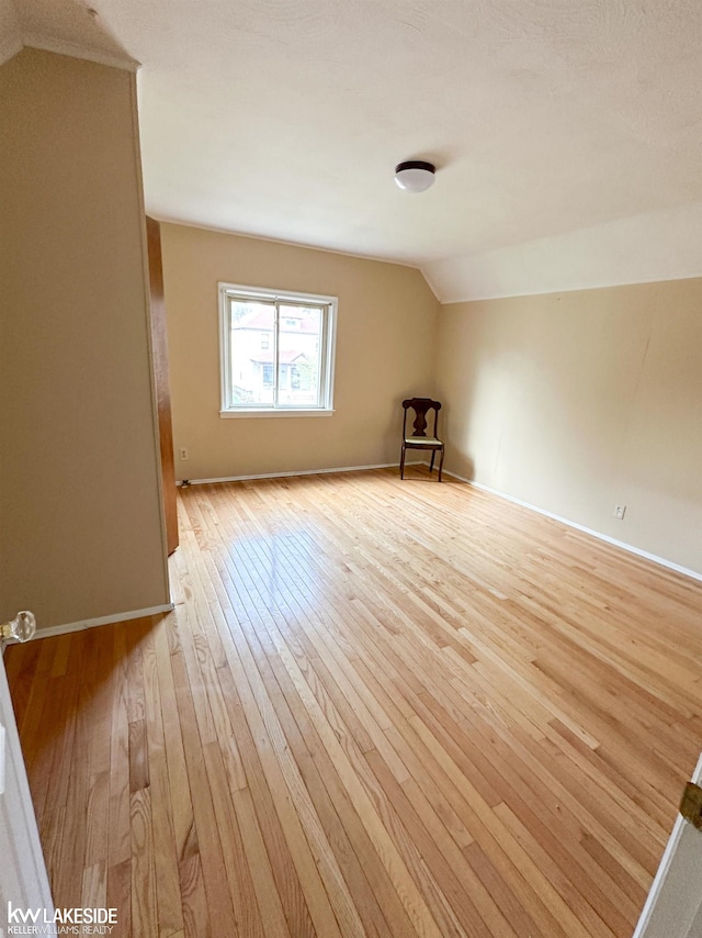 spare room featuring lofted ceiling, light wood-style flooring, and baseboards