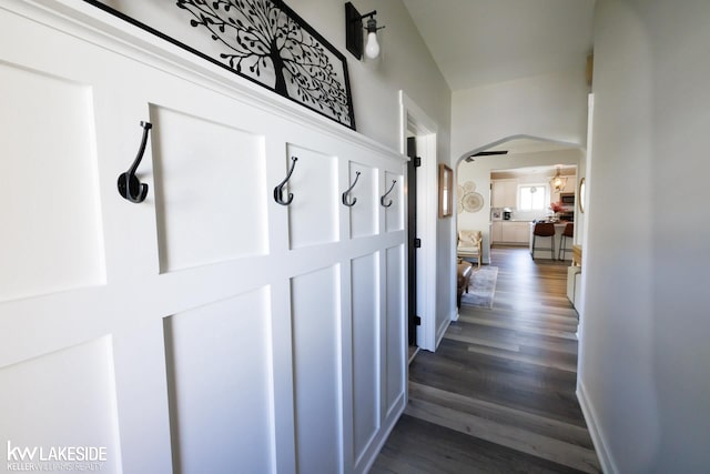 hallway featuring arched walkways, dark wood-style floors, and baseboards