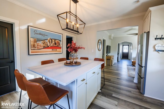 kitchen featuring arched walkways, white cabinets, freestanding refrigerator, a kitchen breakfast bar, and crown molding