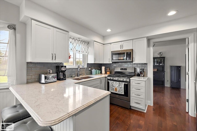 kitchen featuring appliances with stainless steel finishes, a sink, a peninsula, white cabinets, and dark wood-style flooring