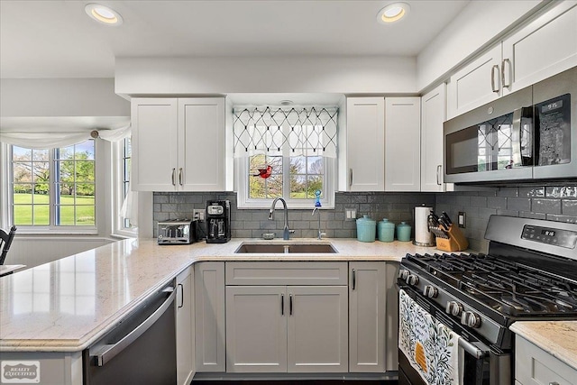 kitchen with stainless steel appliances, a sink, backsplash, a peninsula, and light stone countertops