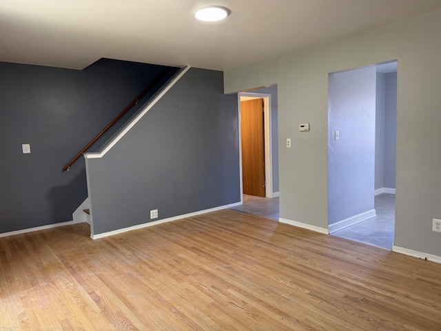 unfurnished living room with stairway, light wood-style flooring, and baseboards