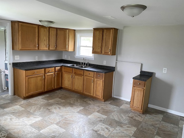 kitchen with a sink, stone finish flooring, brown cabinets, and dark countertops