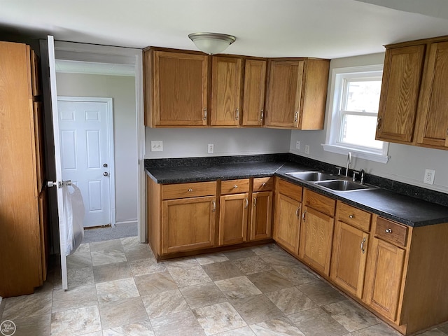 kitchen featuring a sink, brown cabinets, dark countertops, and stone finish floors