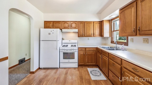 kitchen with white appliances, under cabinet range hood, a sink, and brown cabinets