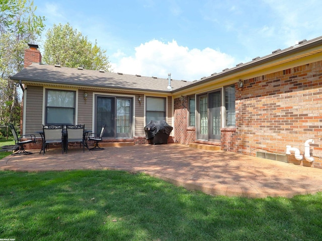 back of property featuring a chimney, a patio, a lawn, and brick siding