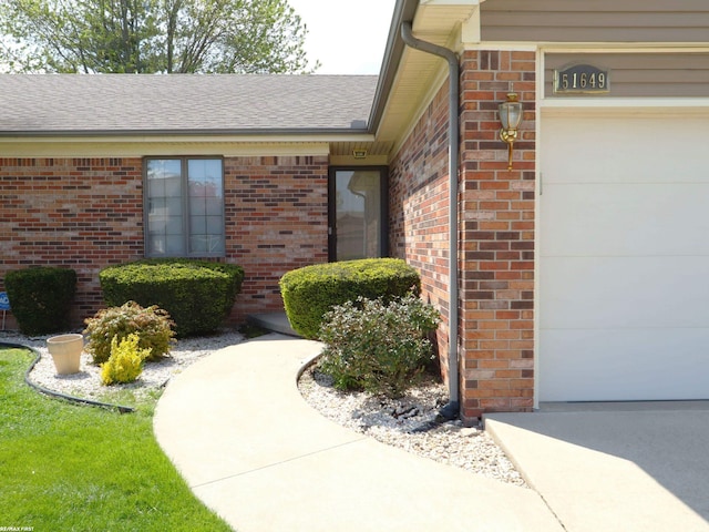 property entrance featuring brick siding, an attached garage, and a shingled roof