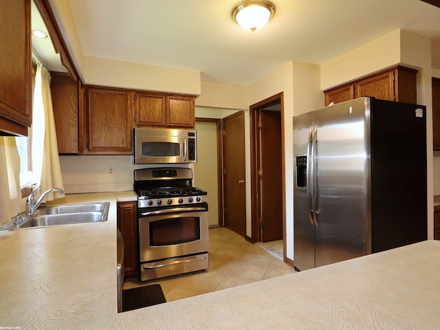 kitchen with stainless steel appliances, a sink, light countertops, light tile patterned flooring, and brown cabinetry